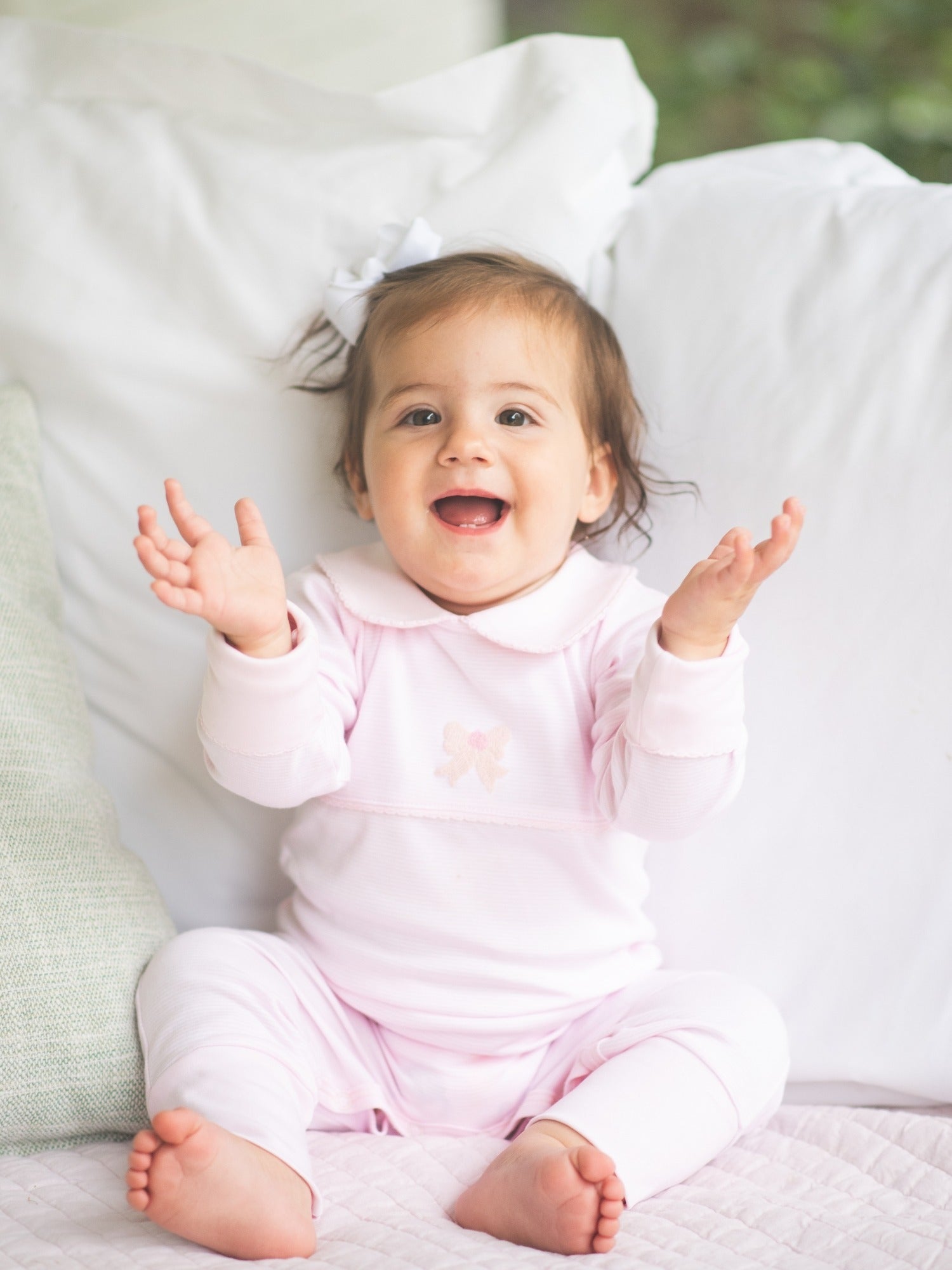 Baby in pink luxury pima playsuit sitting on white couch.