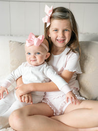 Big sister wearing ruffle pink mini stripe pajamas holding baby sister wearing matching pjs
