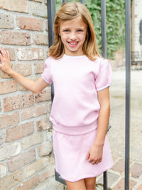 Young girl in a pink quilted Pima cotton shirt set outfit standing against a brick wall.