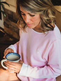Young woman holding coffee and wearing pink pima cotton lounge sweater
