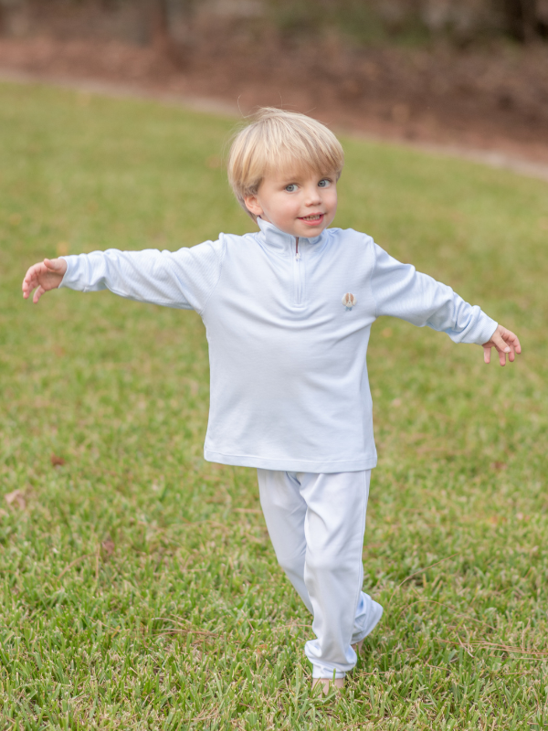 A toddler in a light blue pullover set with a puppy face detail, standing on grass.