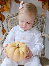 Child holding a small pumpkin in a decorated room with autumn leaves.