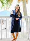 Woman in a navy robe holding a white mug on a balcony with palm trees in the background