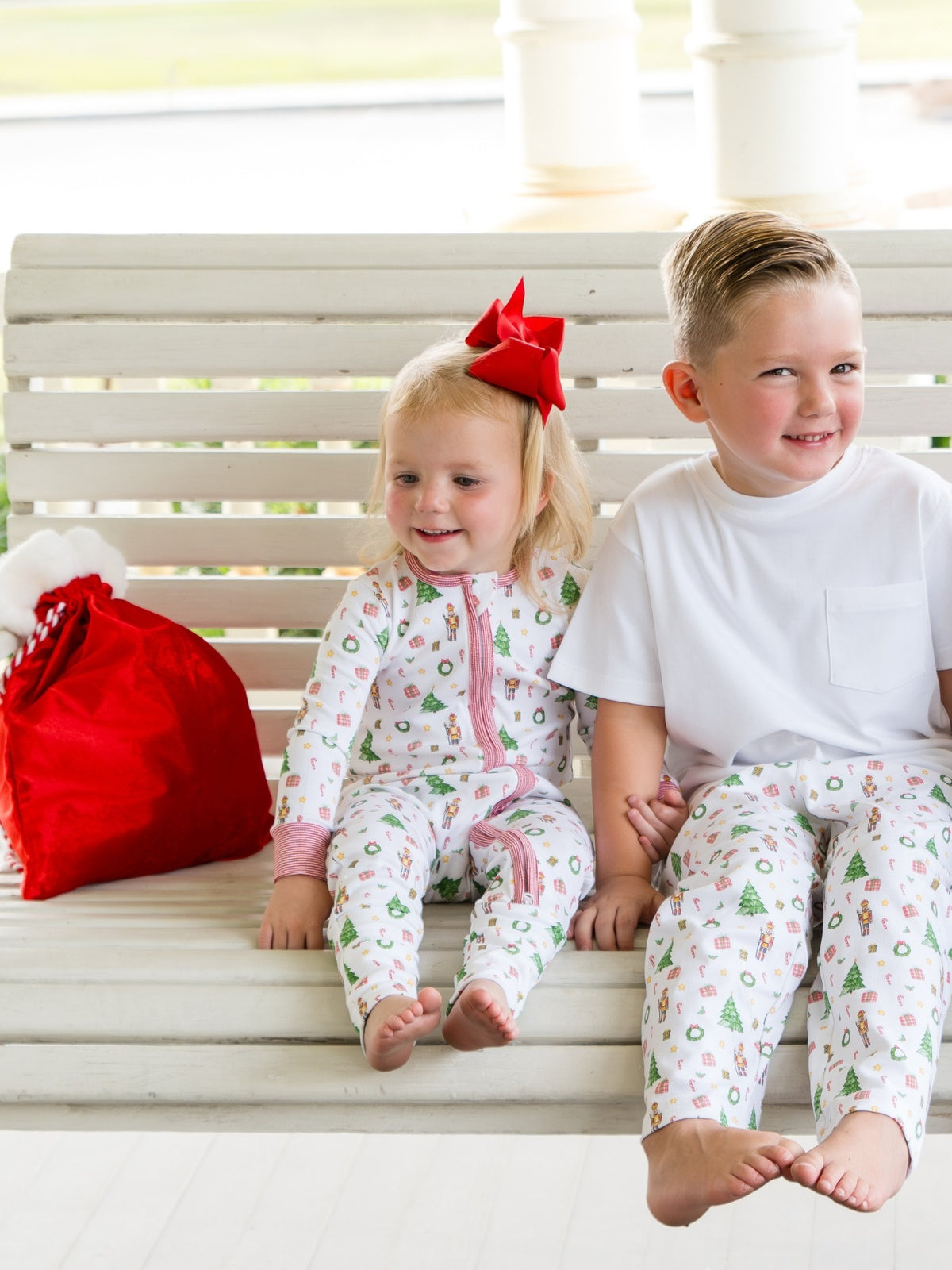 Two children in matching pajamas sitting on a white bench.