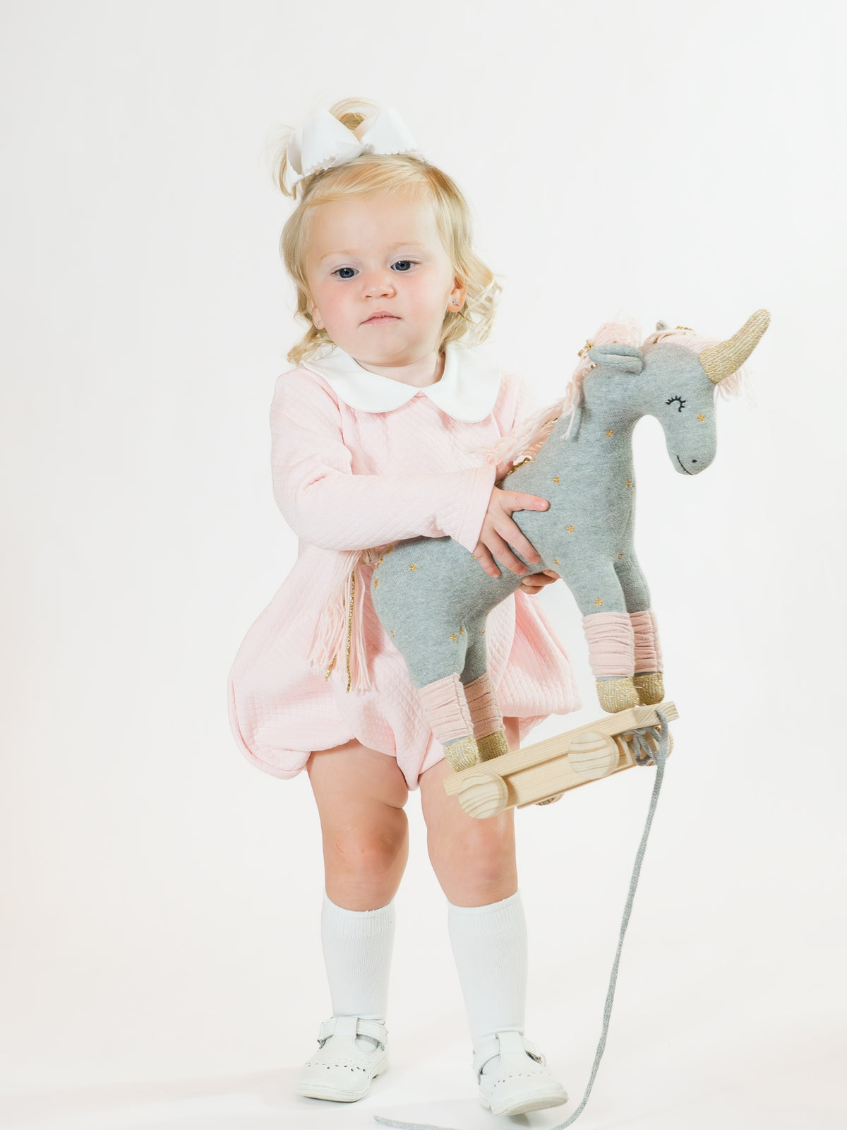 Child holding a plush unicorn toy on a white background wearing Pima cotton pink quilted baby bubble apparel
