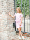Young girl in a pink Pima quilted skirt set outfit standing next to a brick wall and metal gate.