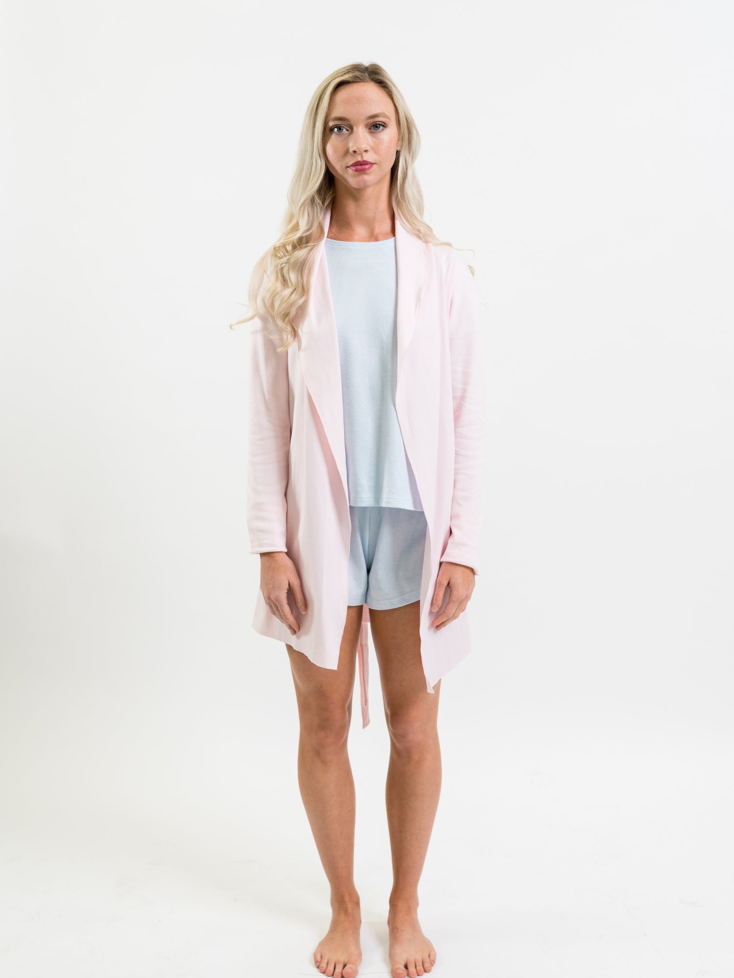 Woman wearing a light pink robe over a light blue lounge set on a white background